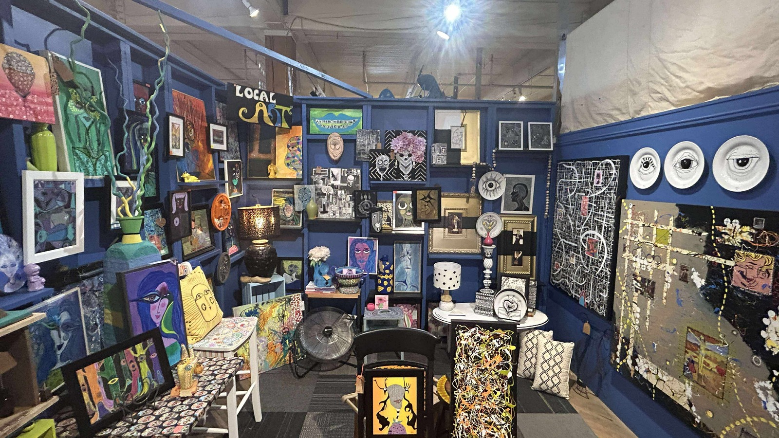 Blue-walled booth filled with paintings, framed pieces, and eclectic art at Midland Arts & Antiques Market in Indianapolis
