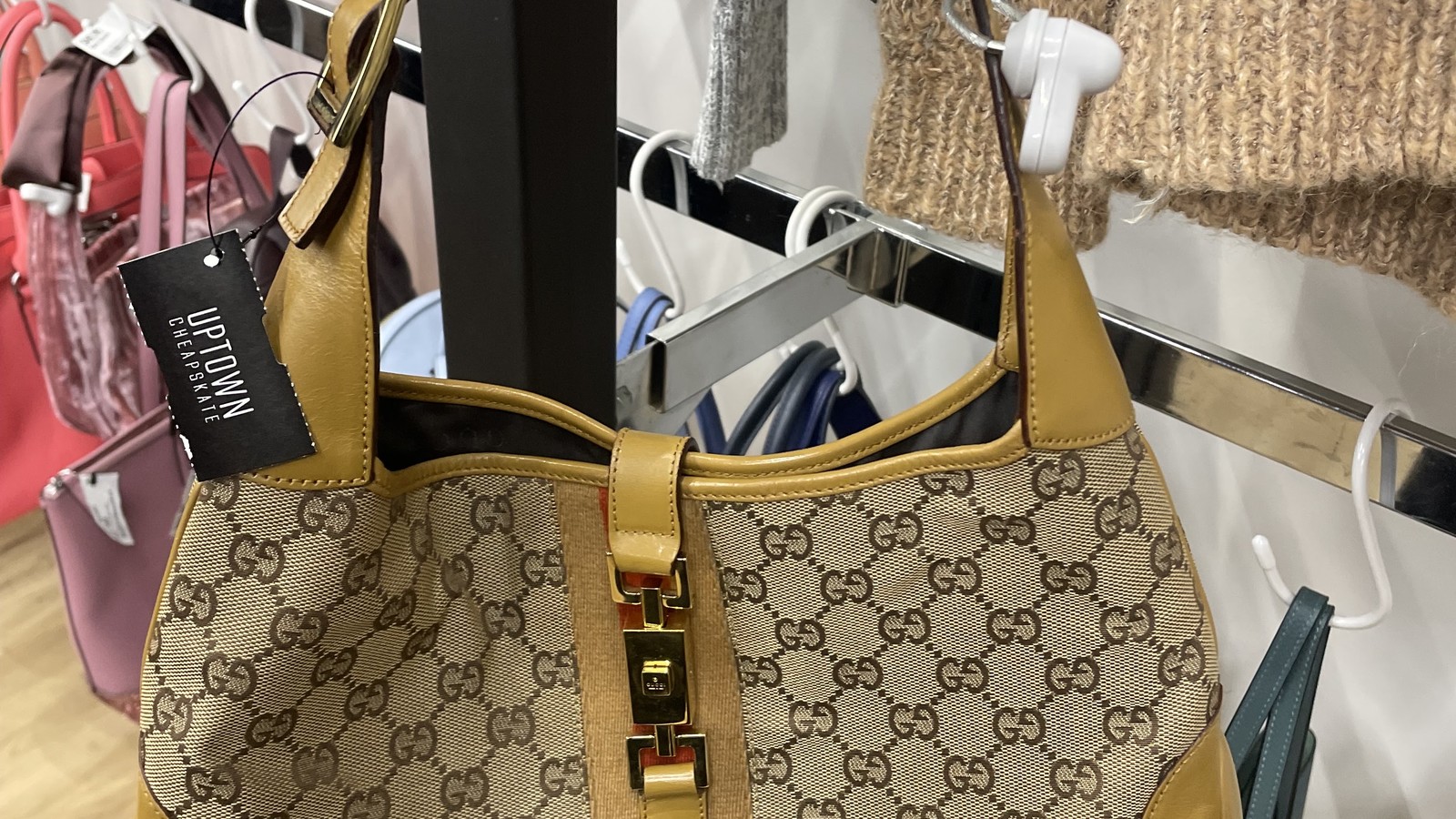 Designer-pattern handbag hanging beside accessory racks at Uptown Cheapskate West York.