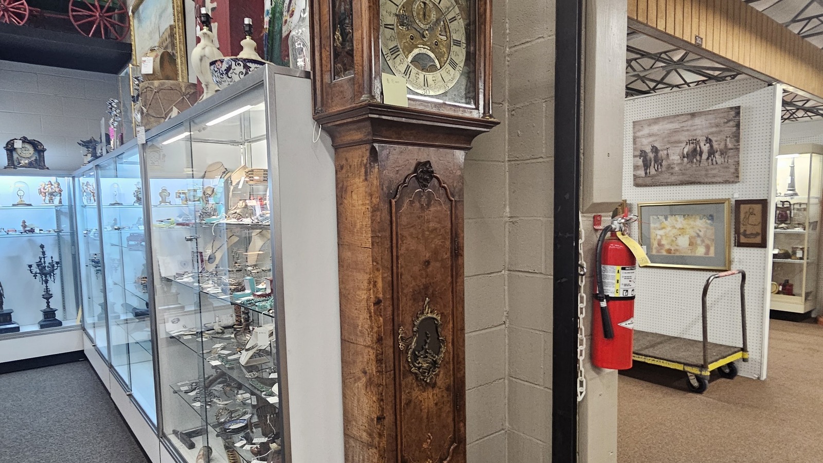 Grandfather clock beside long glass cases filled with smaller antiques