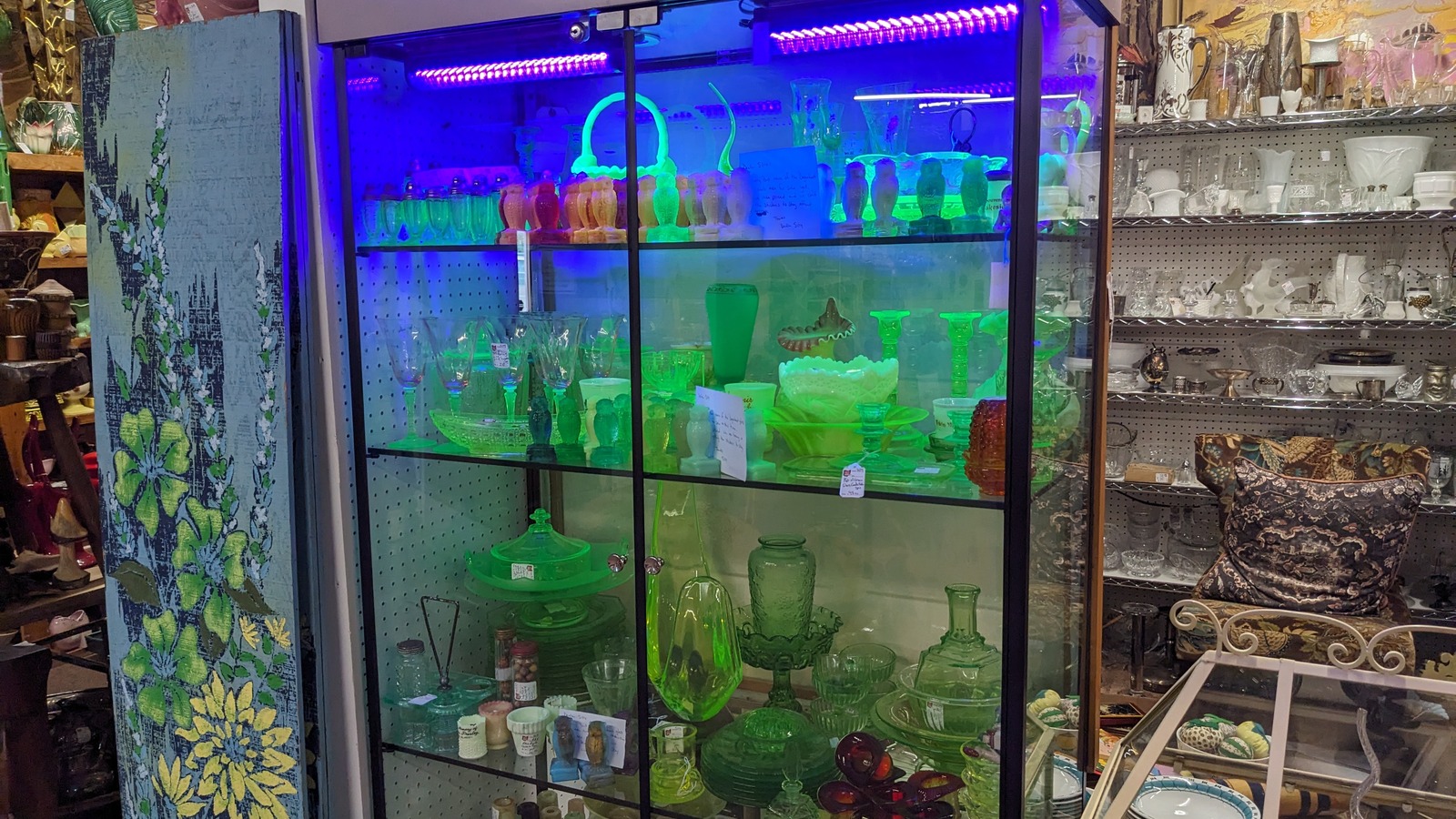 Glowing green glass and lit display cabinets beside clear vintage glassware