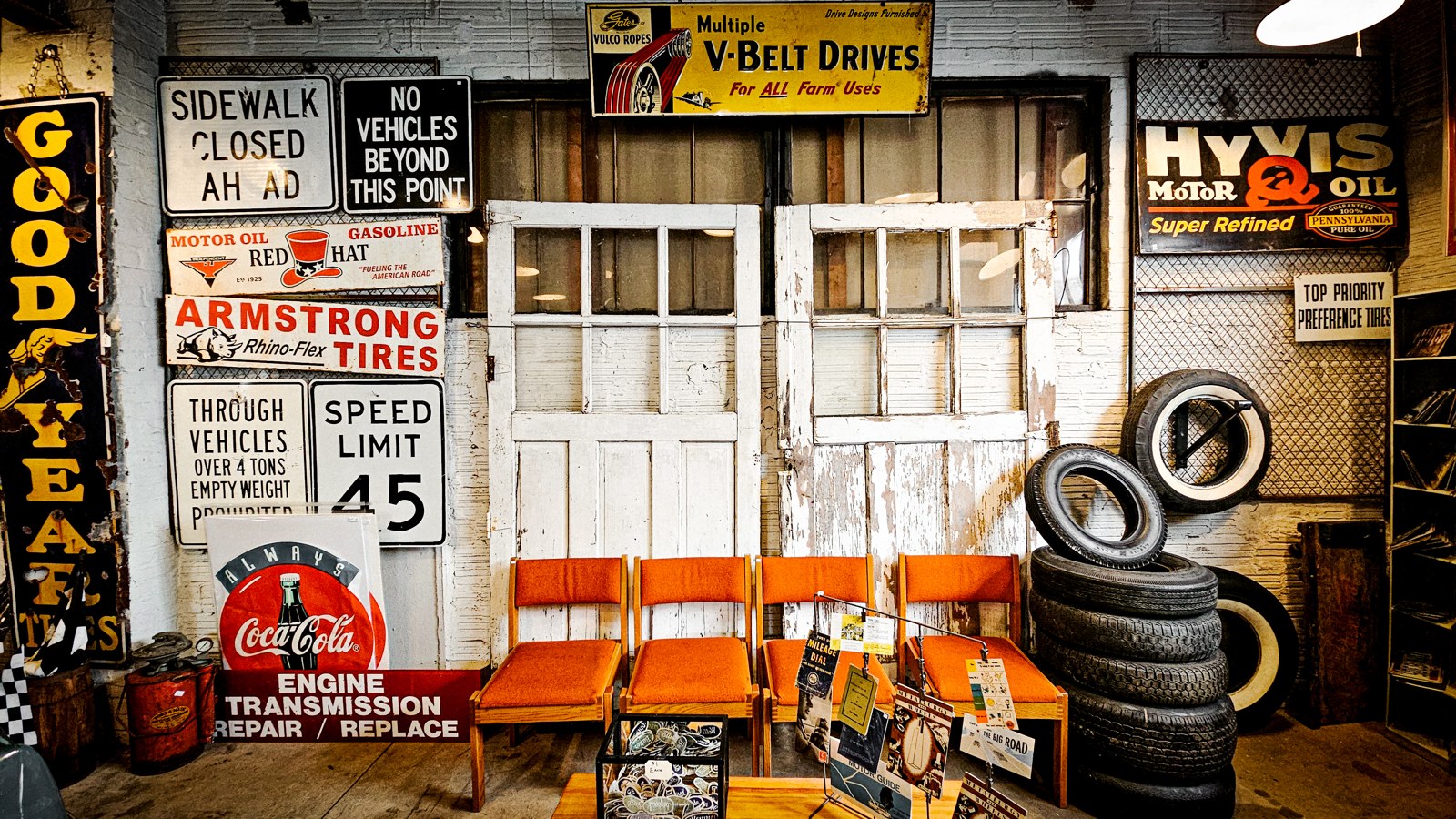 Vintage road signs, service ads, orange chairs, and whitewall tires inside The Bomb Shelter