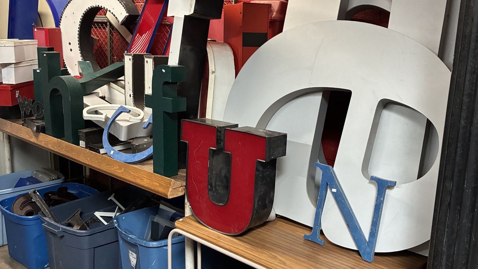 Oversized marquee letters and salvaged sign pieces stacked against a red wall at The Bomb Shelter
