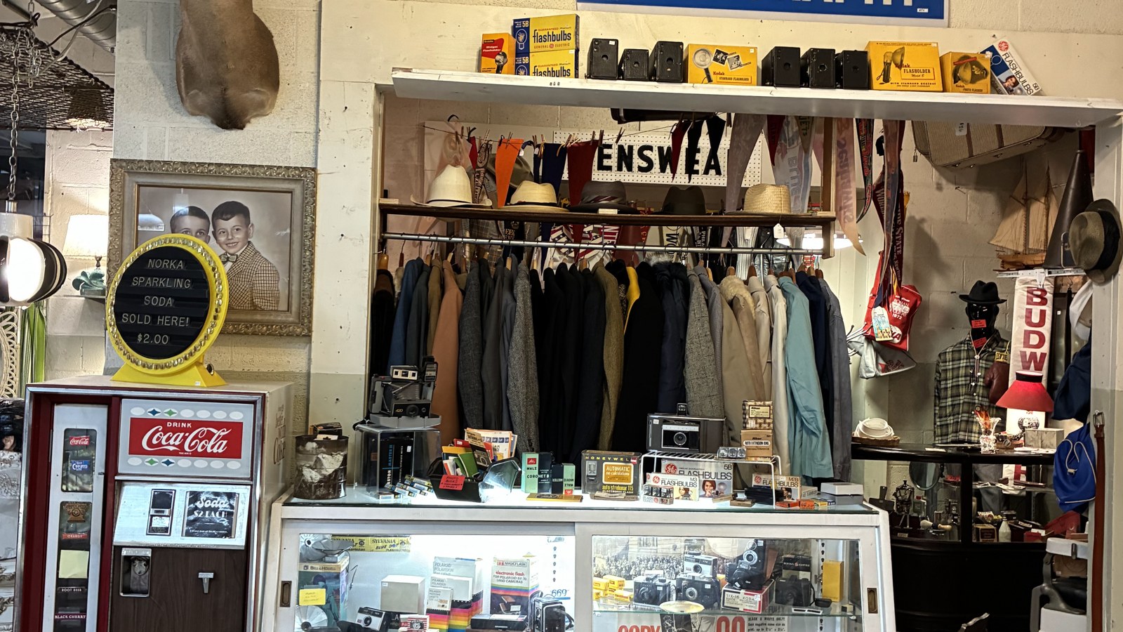 Photography sign above cameras, flashbulbs, jackets, and display cases at The Bomb Shelter