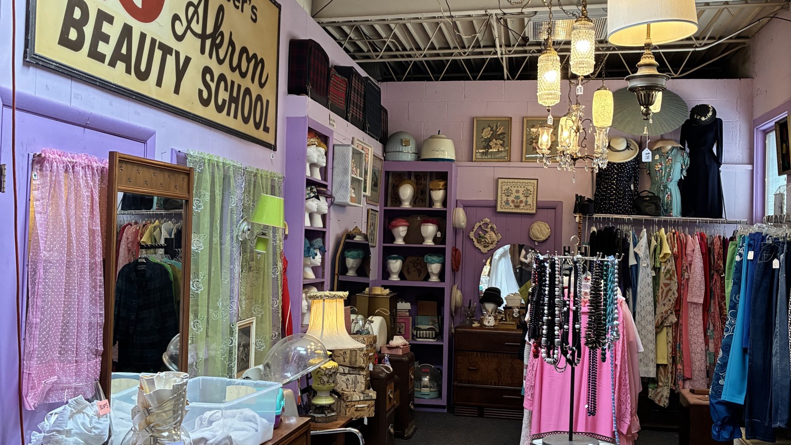 Gerber's Akron Beauty School sign above a vintage clothing room with dresses, hats, and chandeliers