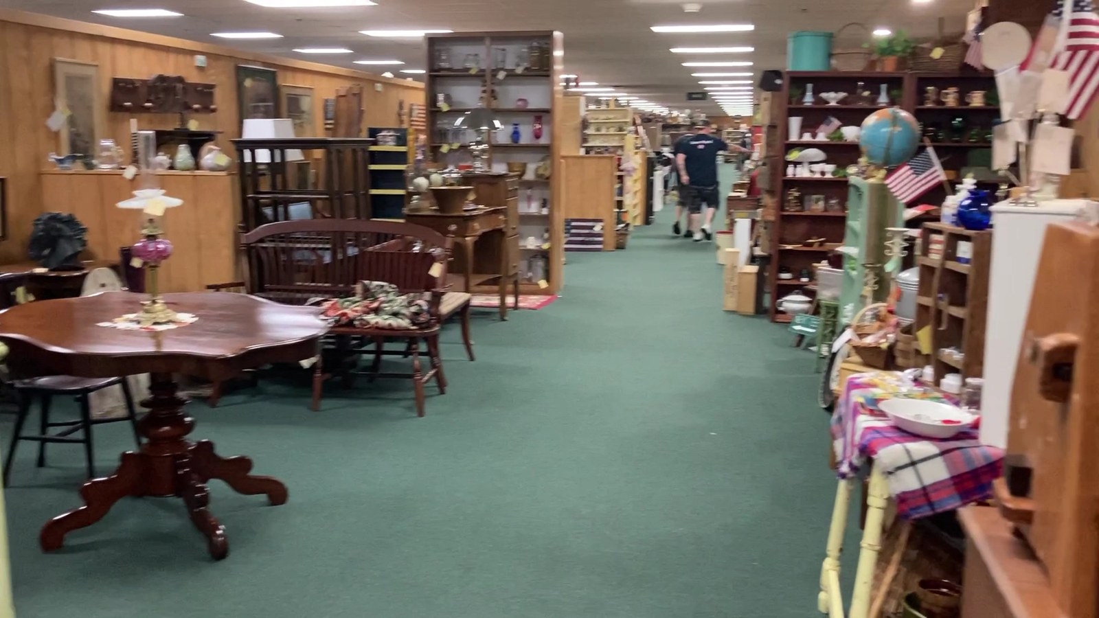Long interior aisle at I-76 Antique Mall lined with display shelves, framed pieces, and antique booths