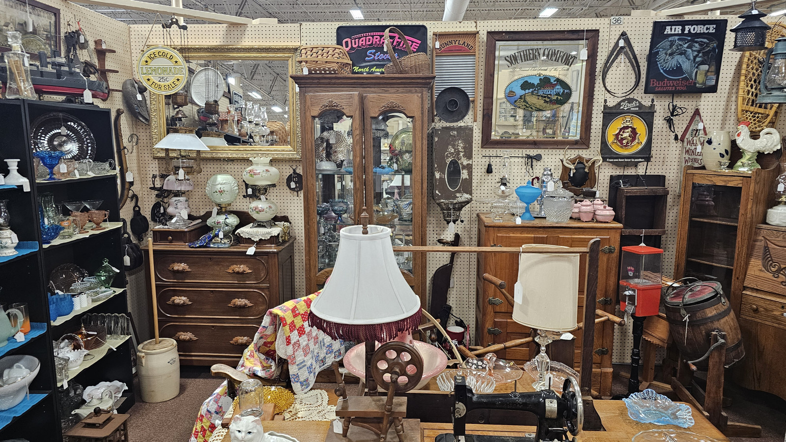 Layered antique booth with lamps, framed art, glassware, and vintage signs at Medina Antique Mall