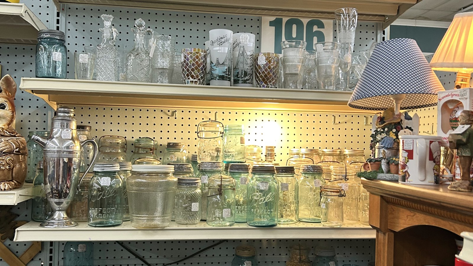 Blue jars, clear glassware, and a lamp-lit shelf display inside Maumee Antique Mall