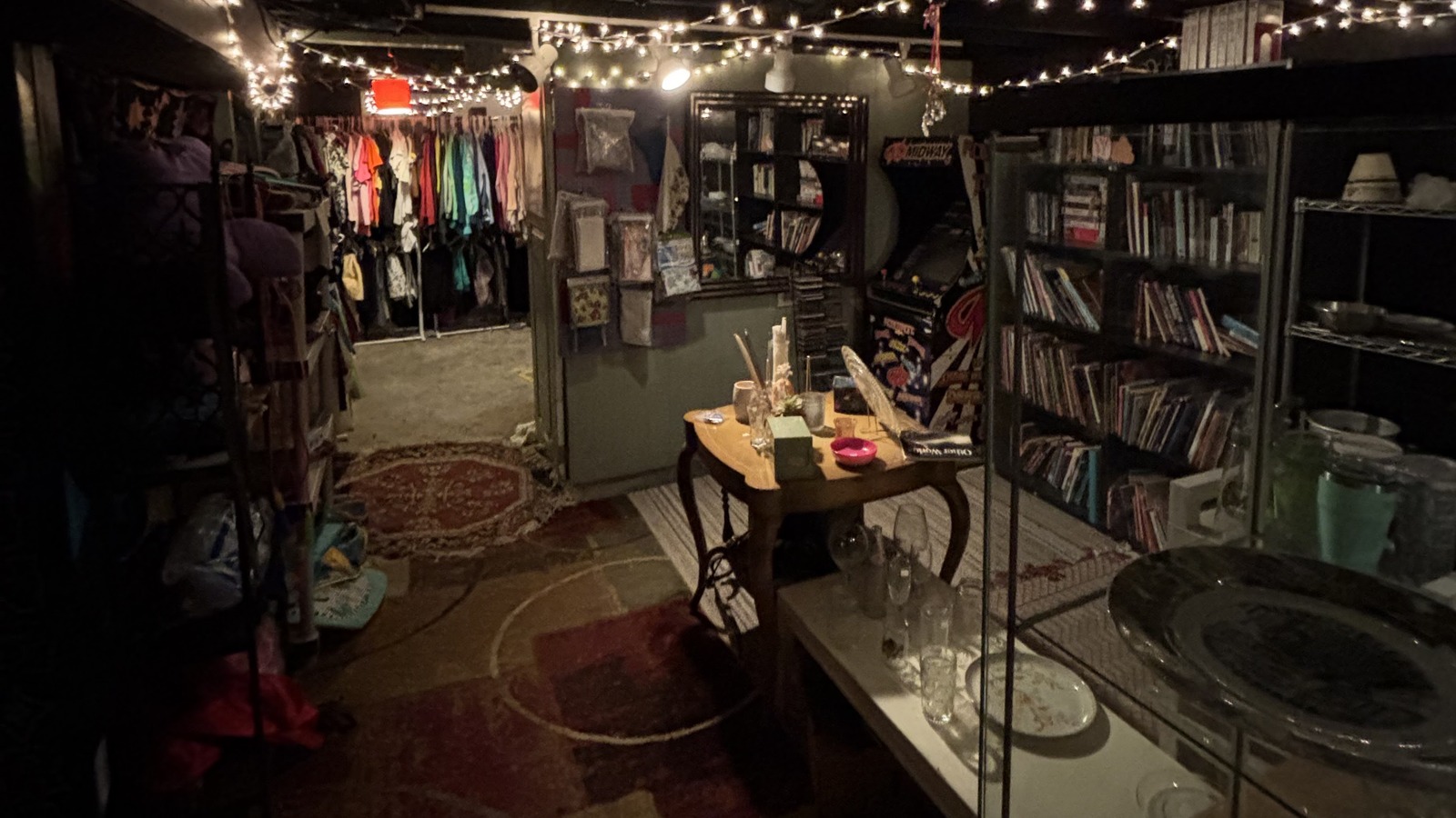 Basement area with string lights, bookshelves, glassware, and clothing at Khlovan's Thrift