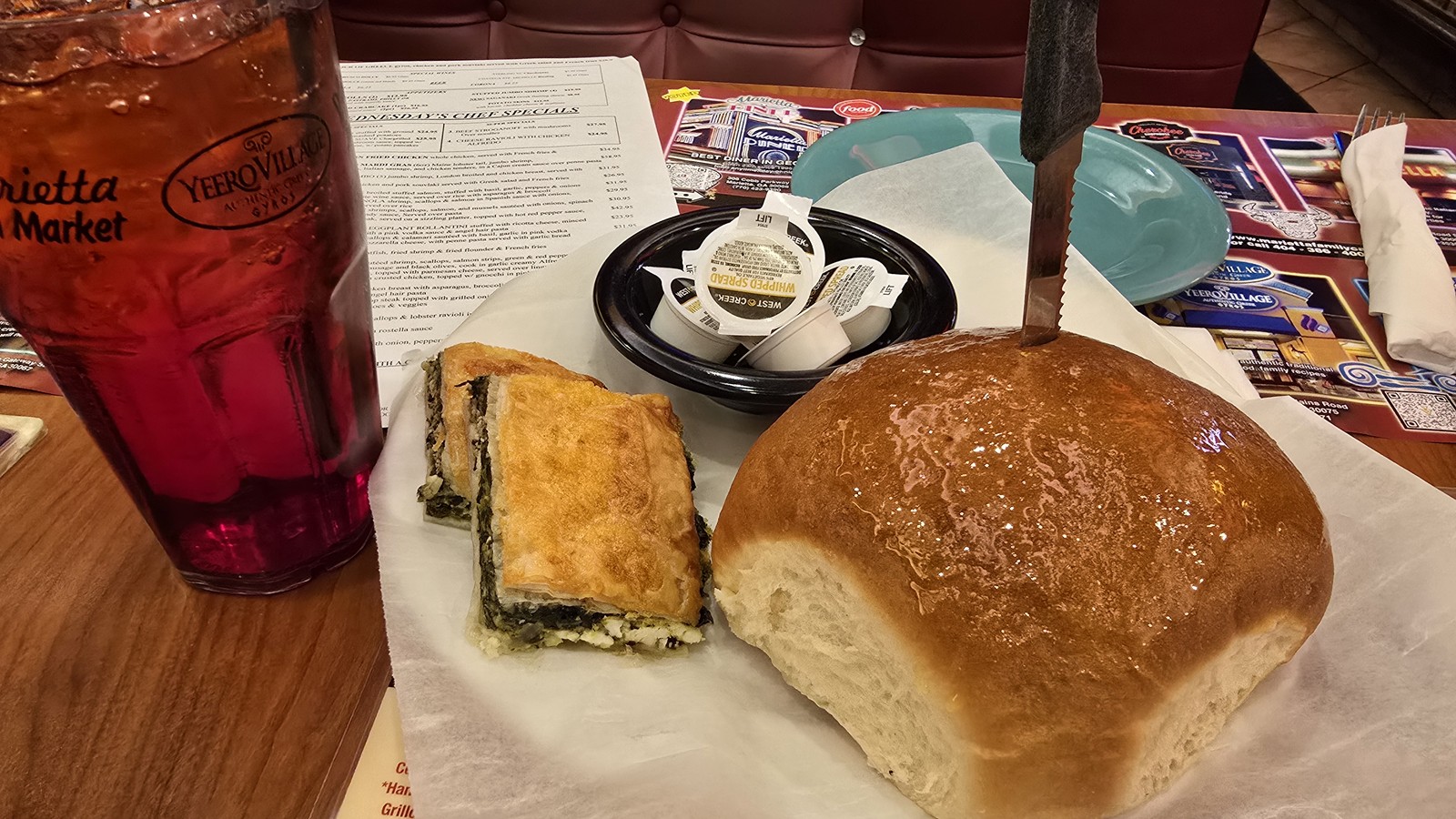 Spinach pie, glossy dinner roll, and iced tea on a booth table at Marietta Diner