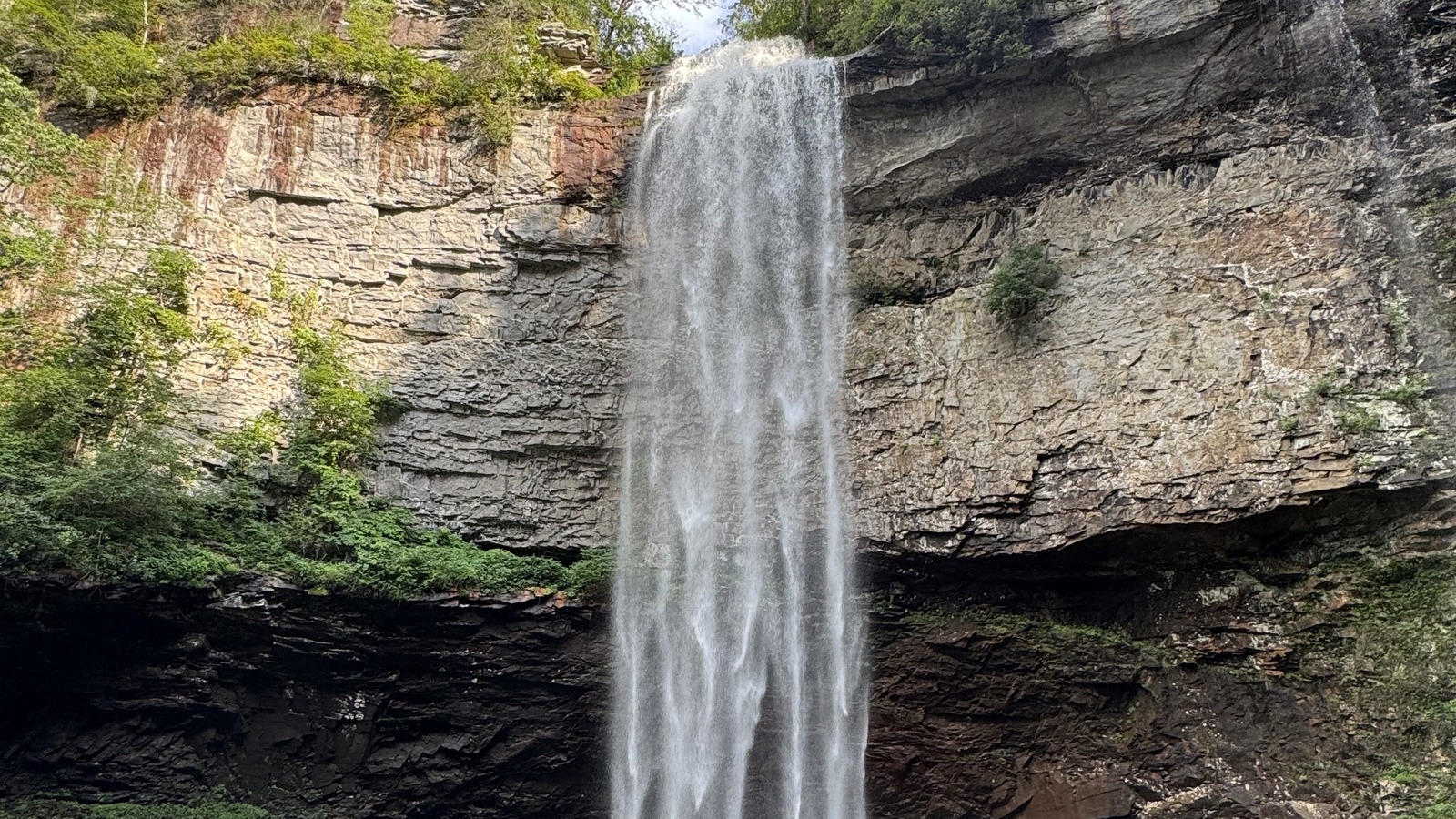 Full white column of Fall Creek Falls dropping beside layered sandstone.