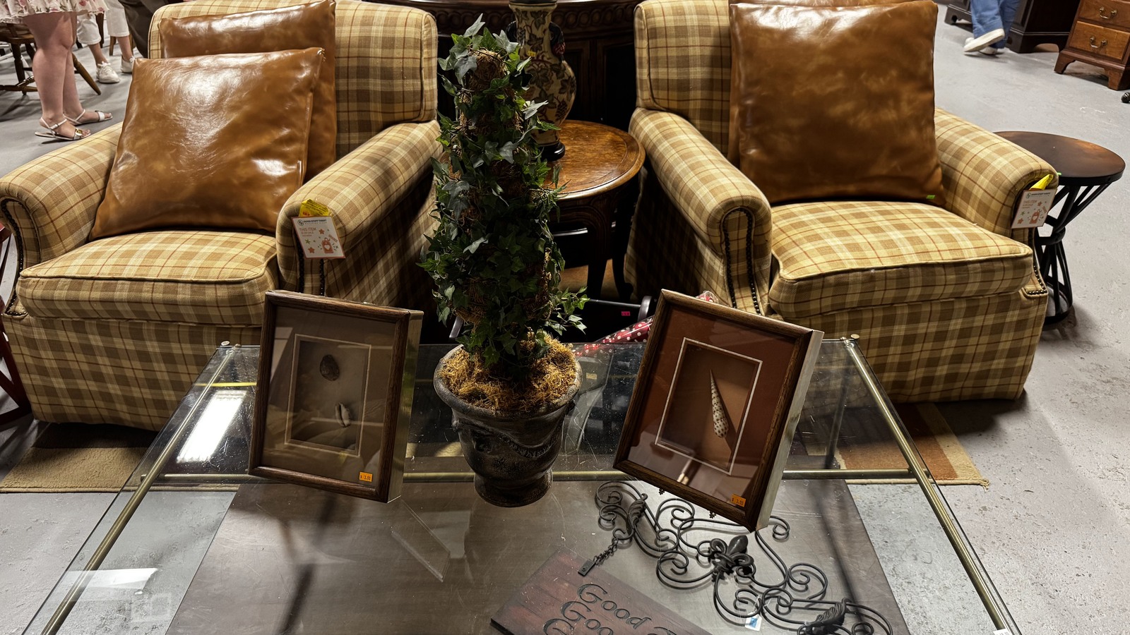 Plaid armchairs, a glass coffee table, and framed art at Good Stuff Thrift