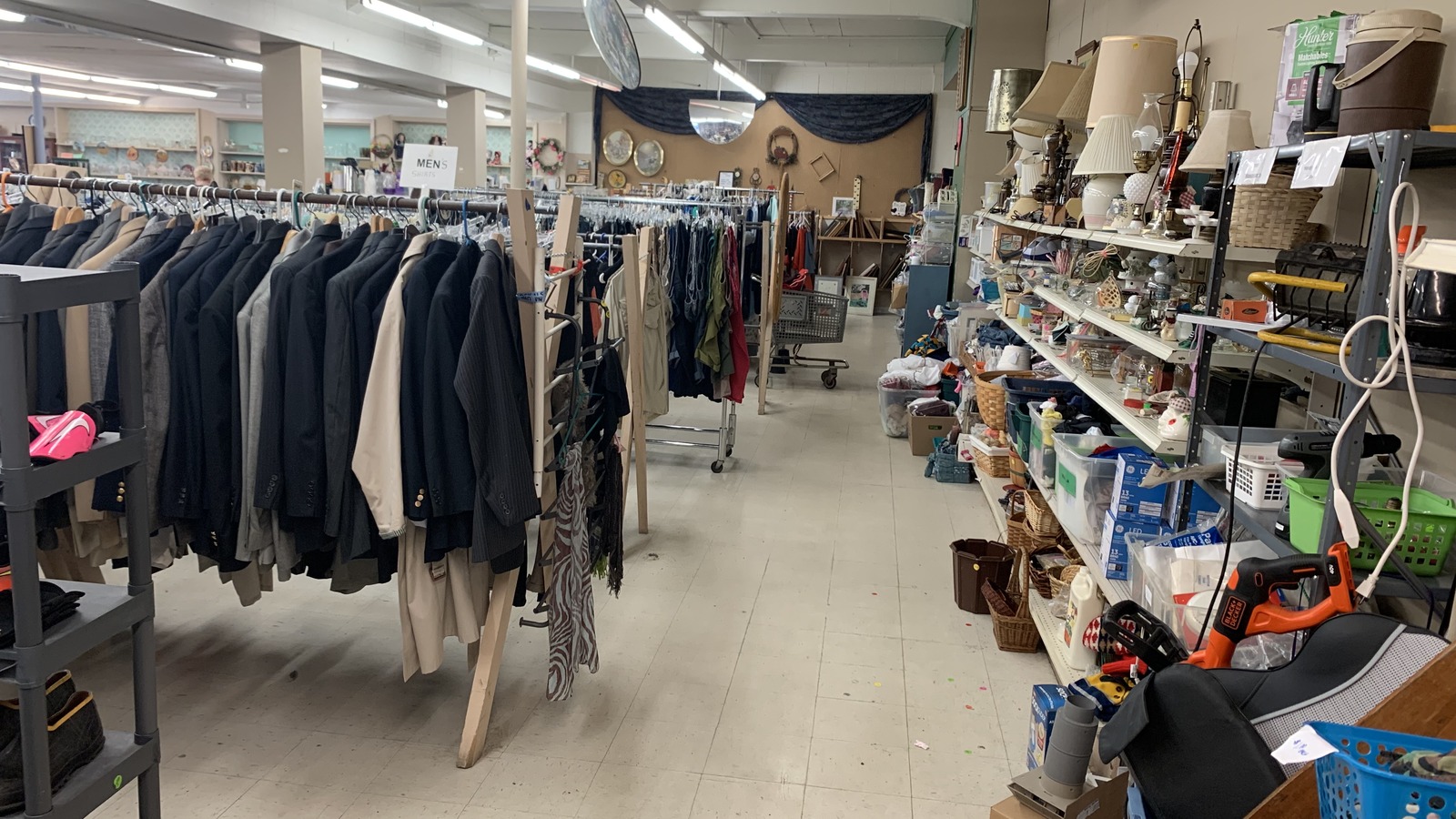 Clothing racks and shelves of housewares inside The Nativity Thrift Store in Rhinelander
